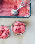 Pink ice cream in a container with two scoops in small bowls on a light background